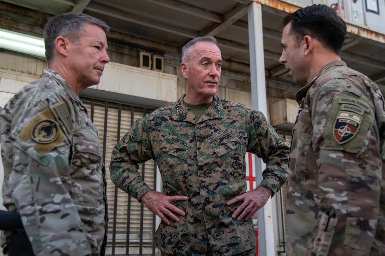 Three service members in camouflage uniforms have a conversation.