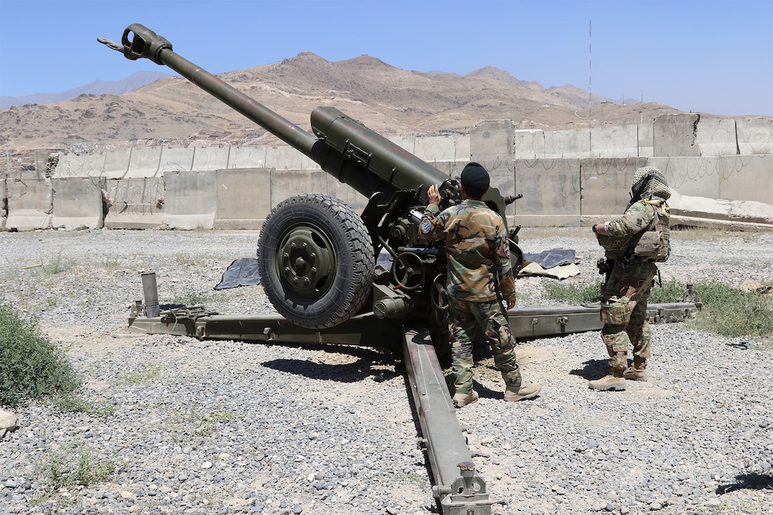 Men stand beside howitzer.