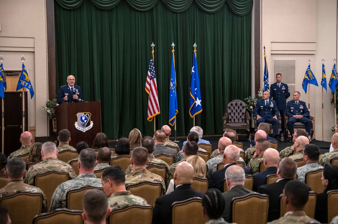 Gen. Arnold Bunch Jr., commander of Air Force Materiel Command, addresses the audience during the Air Force Installation and Mission Support Center change of command July 25 at Joint Base San Antonio-Lackland. Outgoing commander, Maj. Gen. Brad Spacy, and incoming commander, Maj. Gen. Tom Wilcox (right), are seated while Chief Master Sgt. Edwin Ludwigsen, AFIMSC command chief master sergeant, holds the unit flag. (U.S. Air Force photo by Johnny Saldivar)