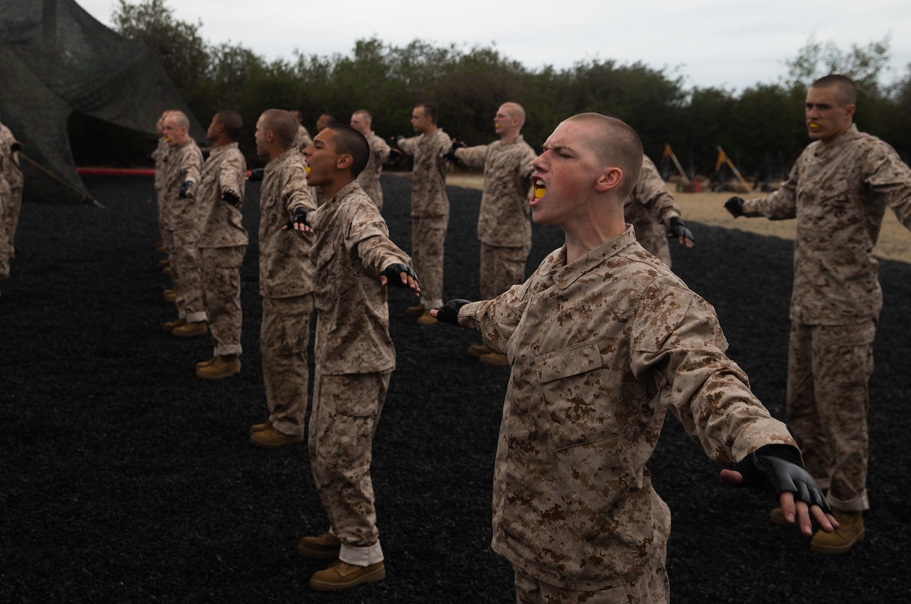 More than a dozen young men in military uniforms stand in formation with their arms outstretched.