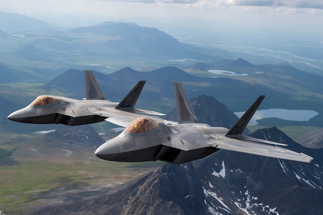 Two planes fly together over mountains.