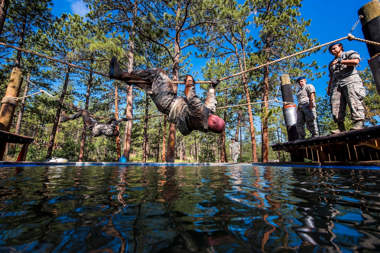 An airman crosses a rope that is over water while other airmen watch.
