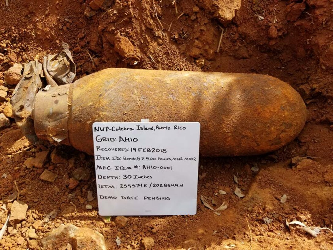 bomb with information written on a white board, NWP-Culebra Island, Puerto Rico; recovered 19FEB2018; Item ID: Bomb, G.P 500-Pound, MK12 MOD2; MEC ITEM#: AH10-0001; Depth: 30 Inches; UTM 254574E/2028549N; Demo Date Pending