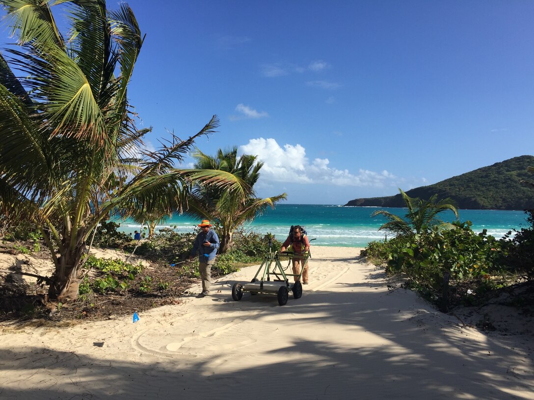 Two men are seen pushing Advanced Geophysical Classification equipment  on Flamenco Beach