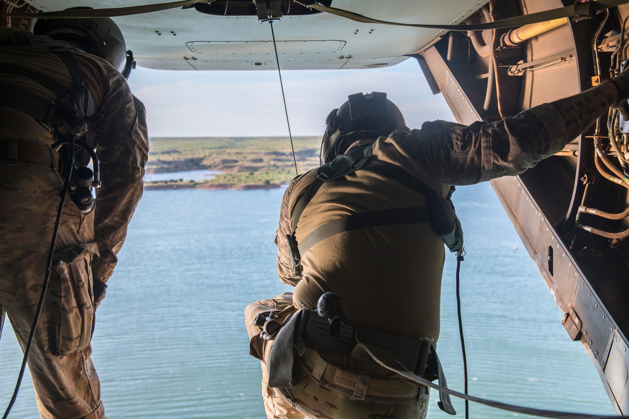 Tech. Sgt. Joseph Sherman, 20th Special Operations Squadron evaluator flight engineer, and Tech. Sgt. Andrew Bostwick, 20th Special Operations Squadron instructor flight engineer, lower a hoist cable to waiting 26th Special Tactics Squadron members below at Ute Lake, N.M., July 23, 2019. During the training, members practiced rappelling from the aircraft and being hoisted into it. (U.S. Air Force photo by Senior Airman Vernon R. Walter III)