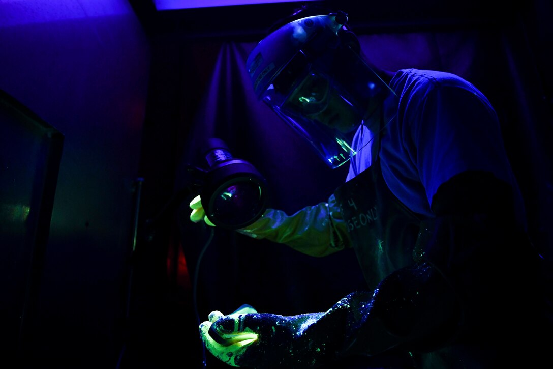 An airmen inspects something using black light.