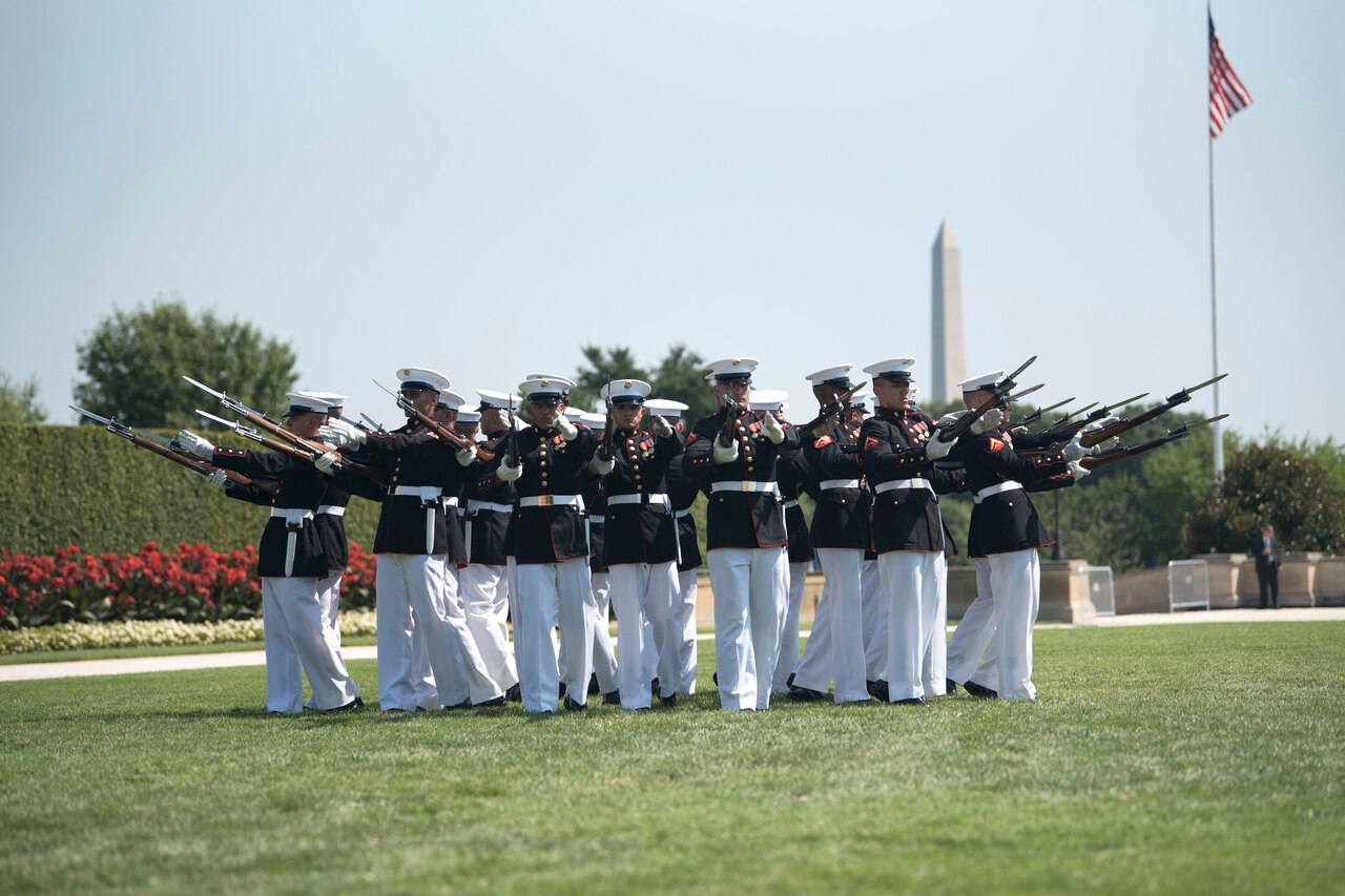 Marines stand in a circular formation and point ceremonial rifles outward.