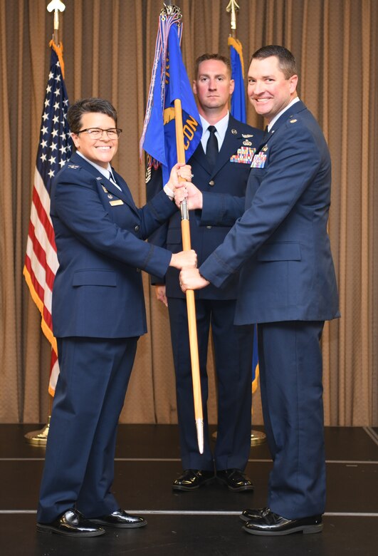 Col Heather Cook, 319th Mission Support Group commander, presents Maj Justin Schneider, 319th Contracting Flight commander, with the 319 CONF guidon during an assumption of command ceremony.