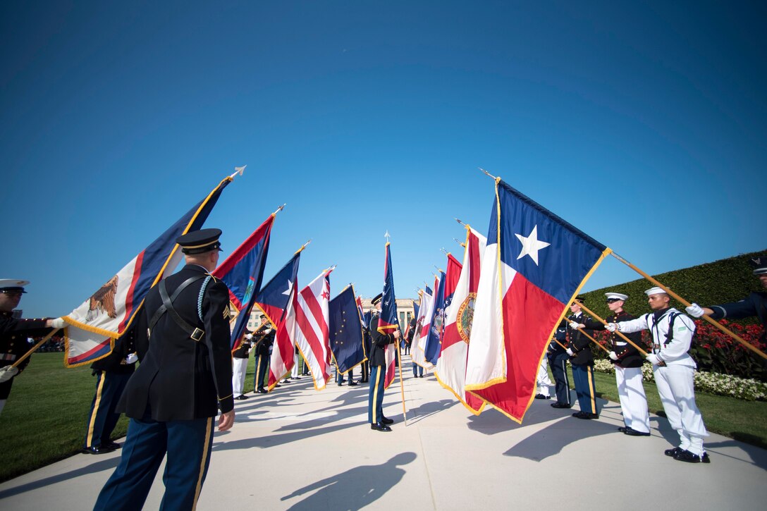 Two rows of service members holding flags while other service members walk between.