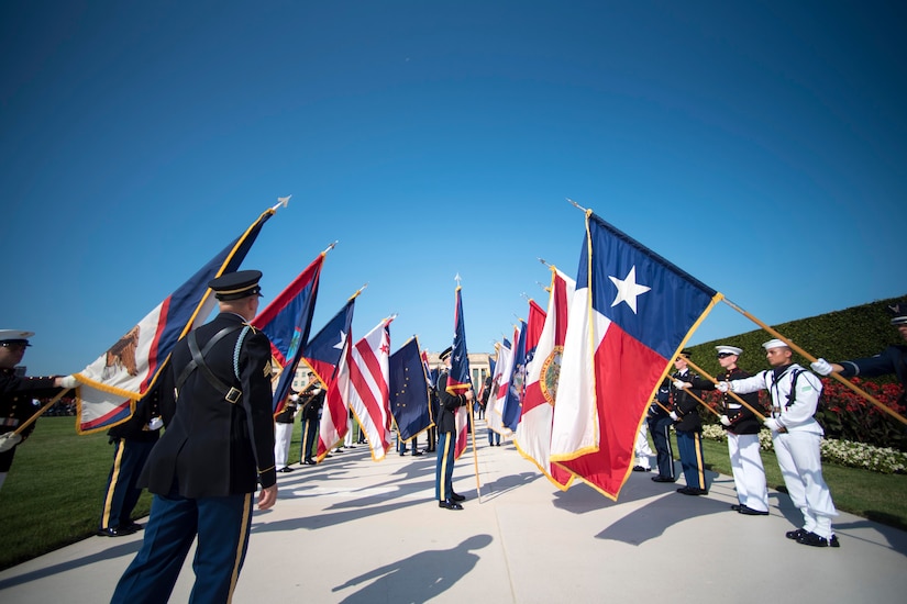 Two rows of service members holding flags while other service members walk between.