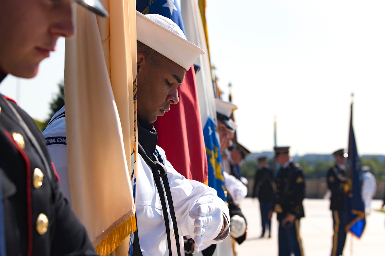 A service member closes his eyes with his head tilted downward; holding a flag.