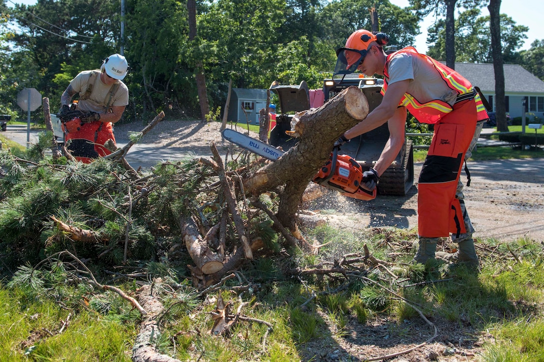 Two airmen saw through a downed tree on a residential street.