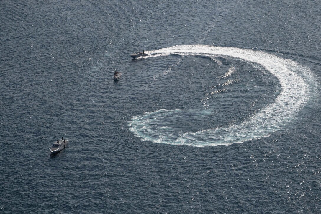 A group of small boats create a circular wake in the ocean.