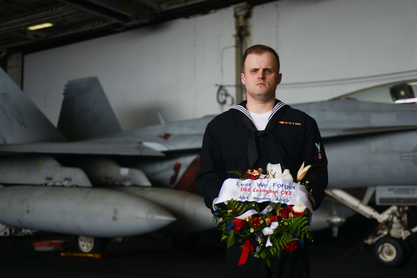 CORAL SEA (July 26, 2019) Religious Program Specialist 3rd Class Johnathan Groves stands with a ceremonial wreath in the hangar bay aboard the Navy’s forward-deployed aircraft carrier USS Ronald Reagan (CVN 76) prior to a remembrance ceremony for USS Lexington (CV 2). Ronald Reagan is the first aircraft carrier to commemorate Lexington since the discovery of the wreckage in 2018. Ronald Reagan, the flagship of Carrier Strike Group 5, provides a combat-ready force that protects and defends the collective maritime interests of its allies and partners in the Indo-Pacific region.