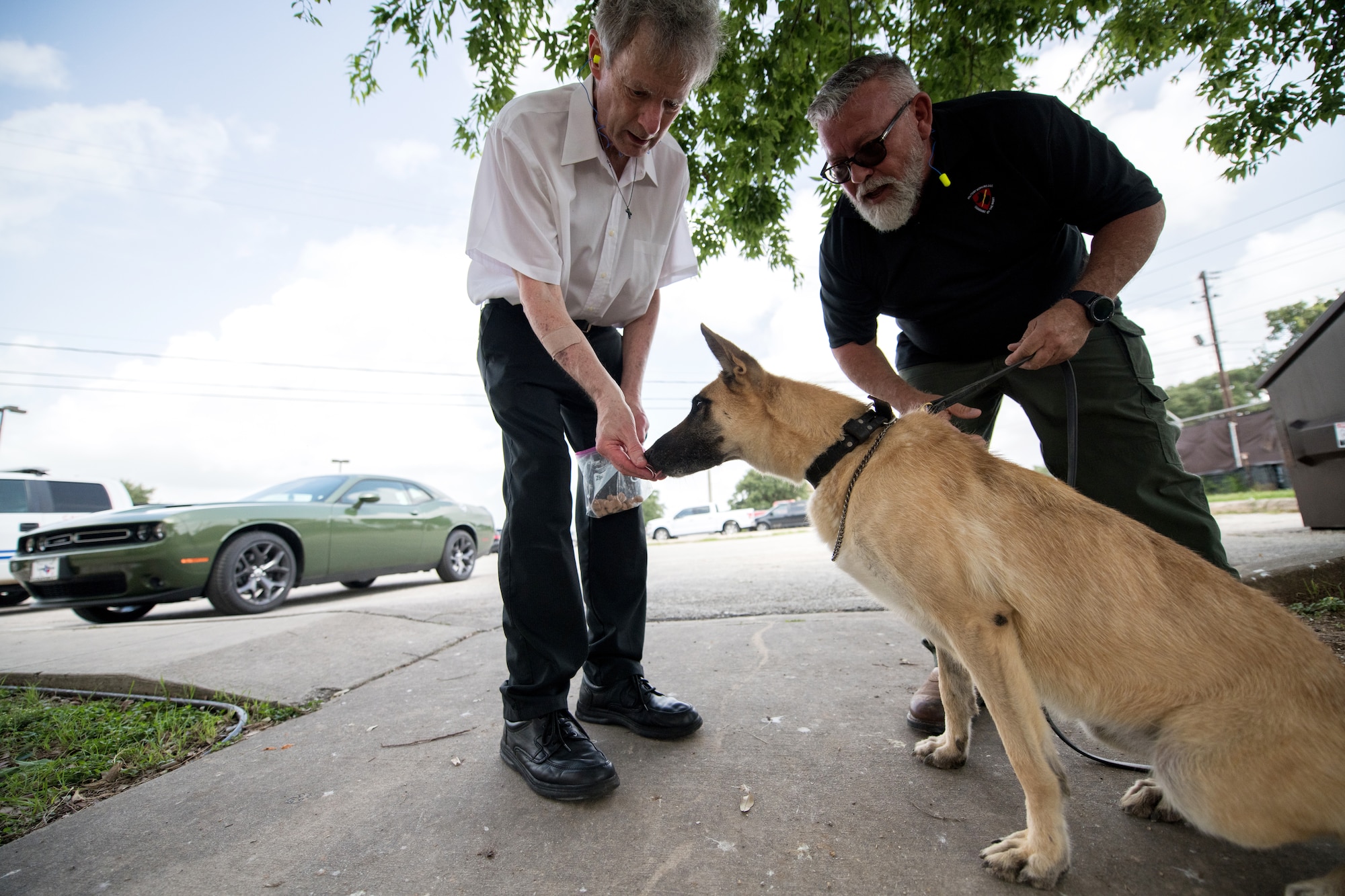 Professor Robert Klesges provides a treat to a military working dog as Jerry Britt, 341st Training Squadron adoptions and dispositions coordinator, monitors its behavior June 26, 2019, at Joint Base San Antonio, Texas.