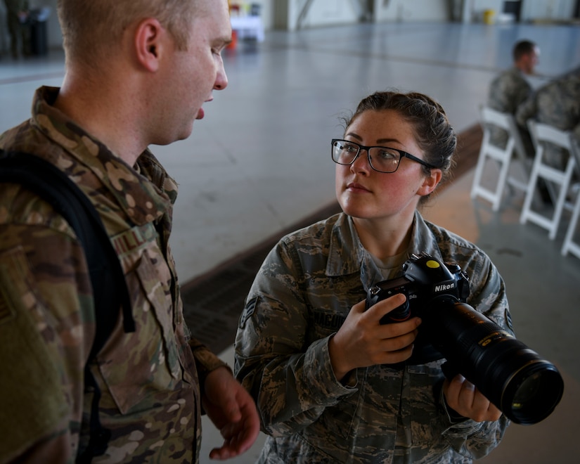 Senior Airman Fawne Maguire, right, an aerospace maintenance journeyman assigned to the 437th Aircraft Maintenance Squadron, shadows Senior Airman Cody Miller, a photojournalist assigned to the Joint Base Charleston Public Affairs Office, to learn more about public affairs during a change of command ceremony at Joint Base Charleston, S.C. July 12, 2019. Maguire said she is interested in retraining out of her current career field and into the public affairs, comptroller, personnel, manpower and aviation resource management career fields. She was able to learn more about the career fields by shadowing members of each job.