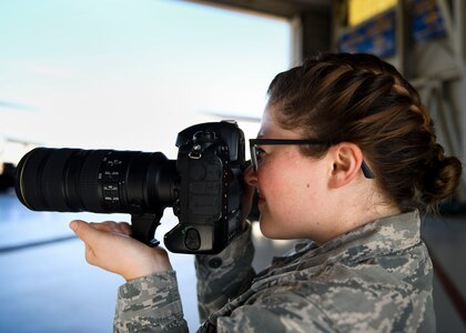 Senior Airman Fawne Maguire, an aerospace maintenance journeyman assigned to the 437th Aircraft Maintenance Squadron, practices taking photos at a change of command ceremony at Joint Base Charleston, S.C. July 12, 2019. Maguire said she is interested in retraining out of her current career field and into the public affairs, comptroller, personnel, manpower and aviation resource management career fields. She was able to learn more about the career fields by shadowing members of each job.