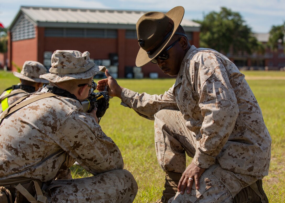 Marksmanship Instructor Sgt. Cedricxavier Hart helps a recruit with  Golf Company, 2nd Recruit Training Battalion, sight in to his Rifle Combat Optic during grass week on Marine Corps Recruit Depot Parris Island, S.C. July 25, 2019. Grass week teaches recruits shooting positions and weapon safety rules for tables 1 and 2. Hart is a native of Nashville, Tennessee. (U.S. Marine Corps photo by Cpl. Isabella Ortega)