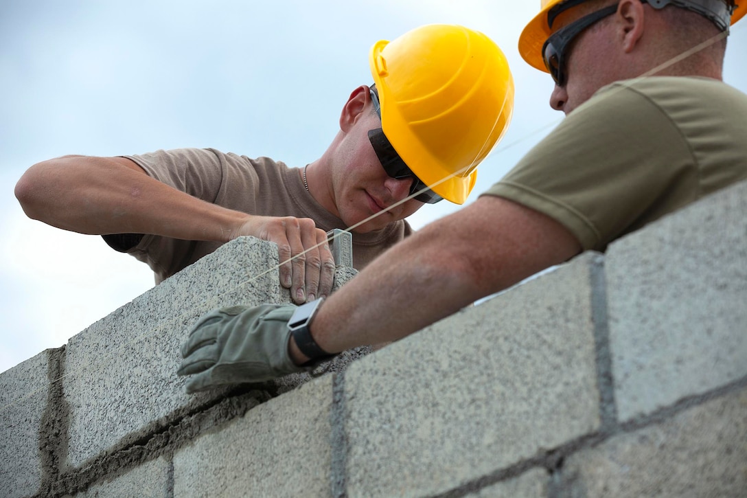 Two soldiers lay cinder blocks to build a wall.