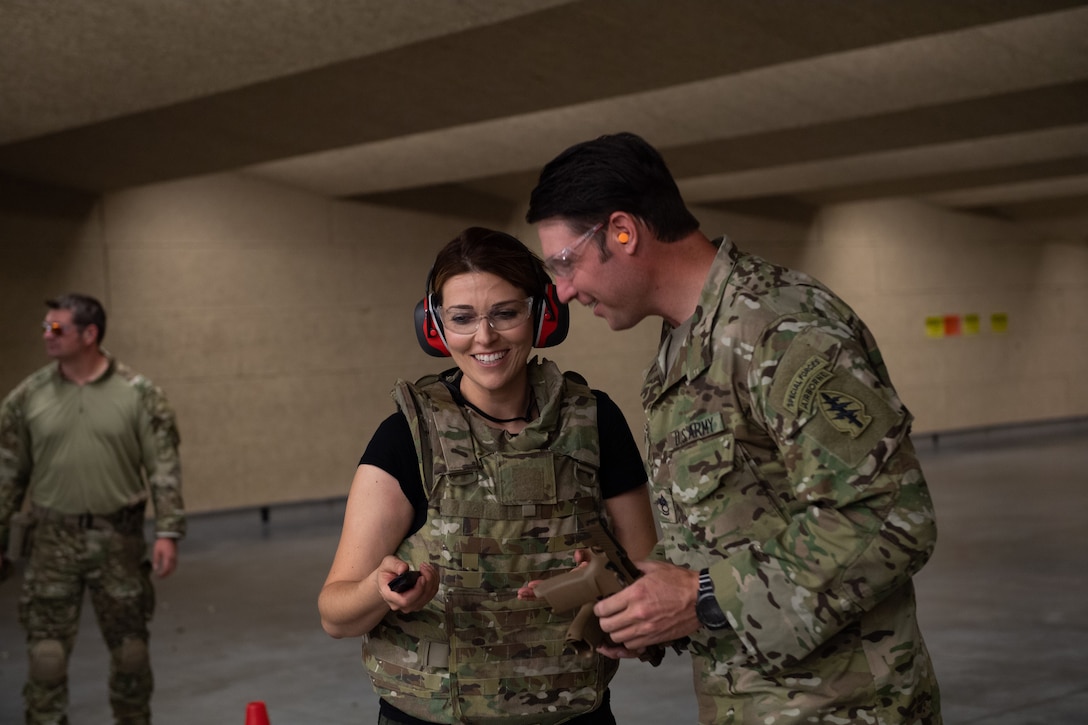 A soldier talks to a civilian wearing a protective vest and earphones.