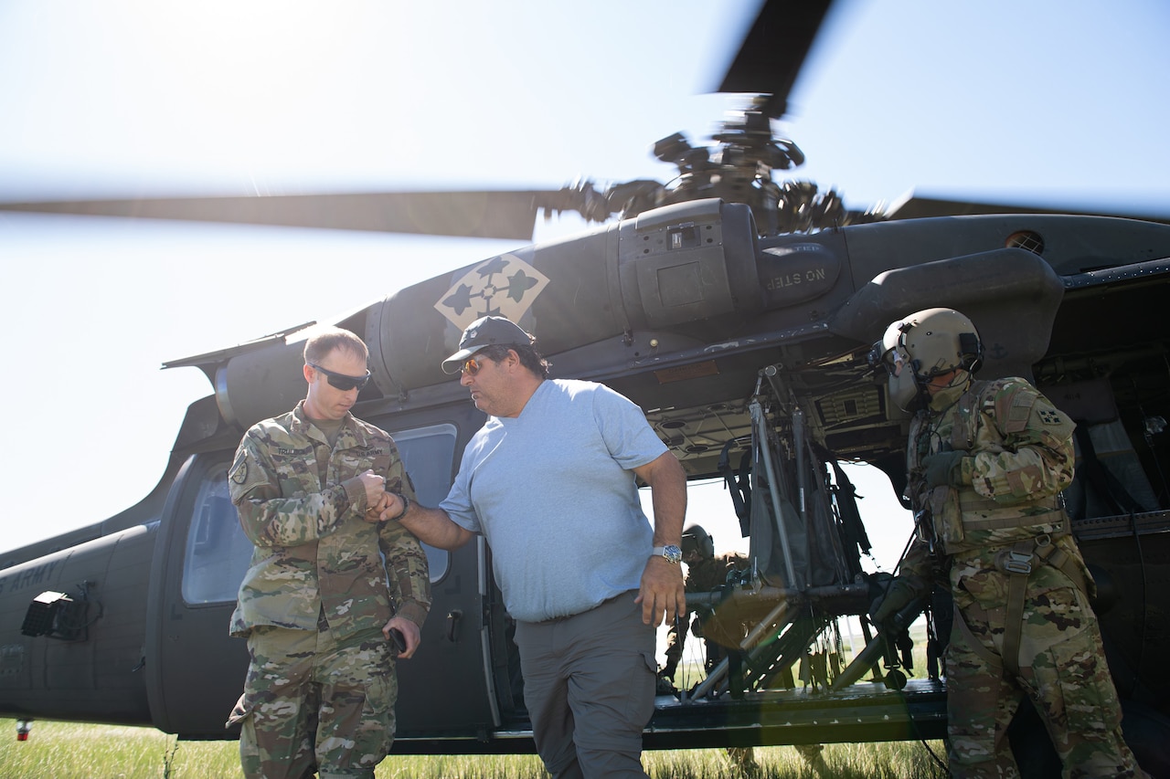 A civilian fist-bumps a soldier outside a helicopter.