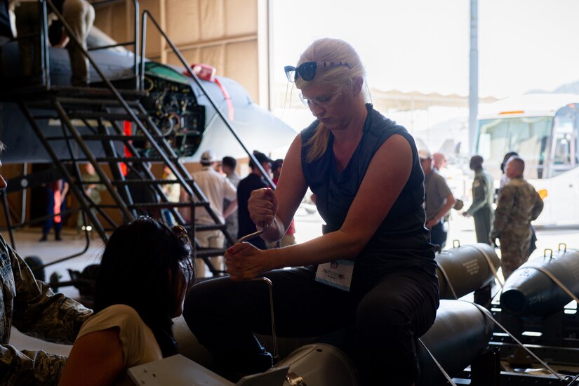 A civilian sits atop a projectile in a hangar-type space and works on it with a tool.