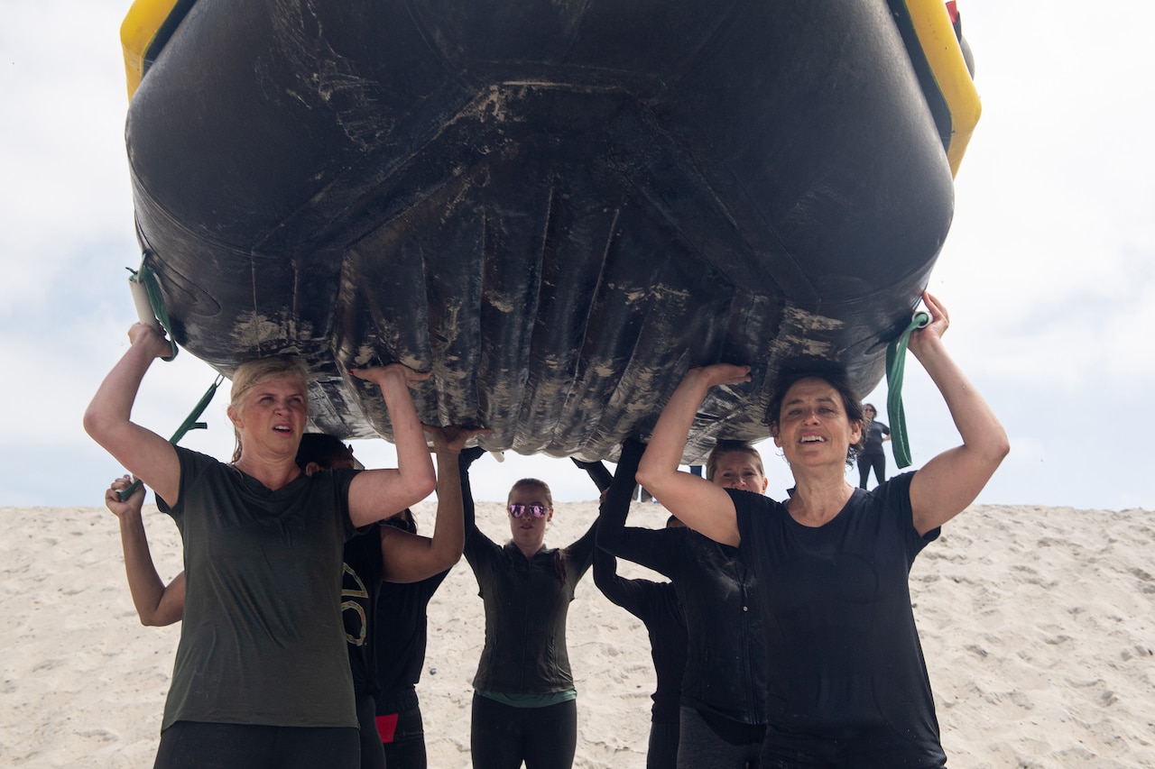 Civilians walk on a beach holding a rubber boat over their heads.