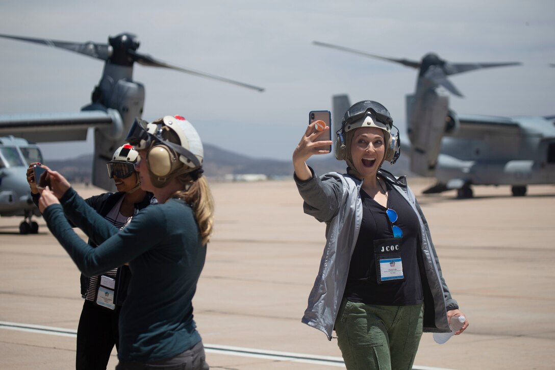 A woman takes a selfie in front of an aircraft while others look on.