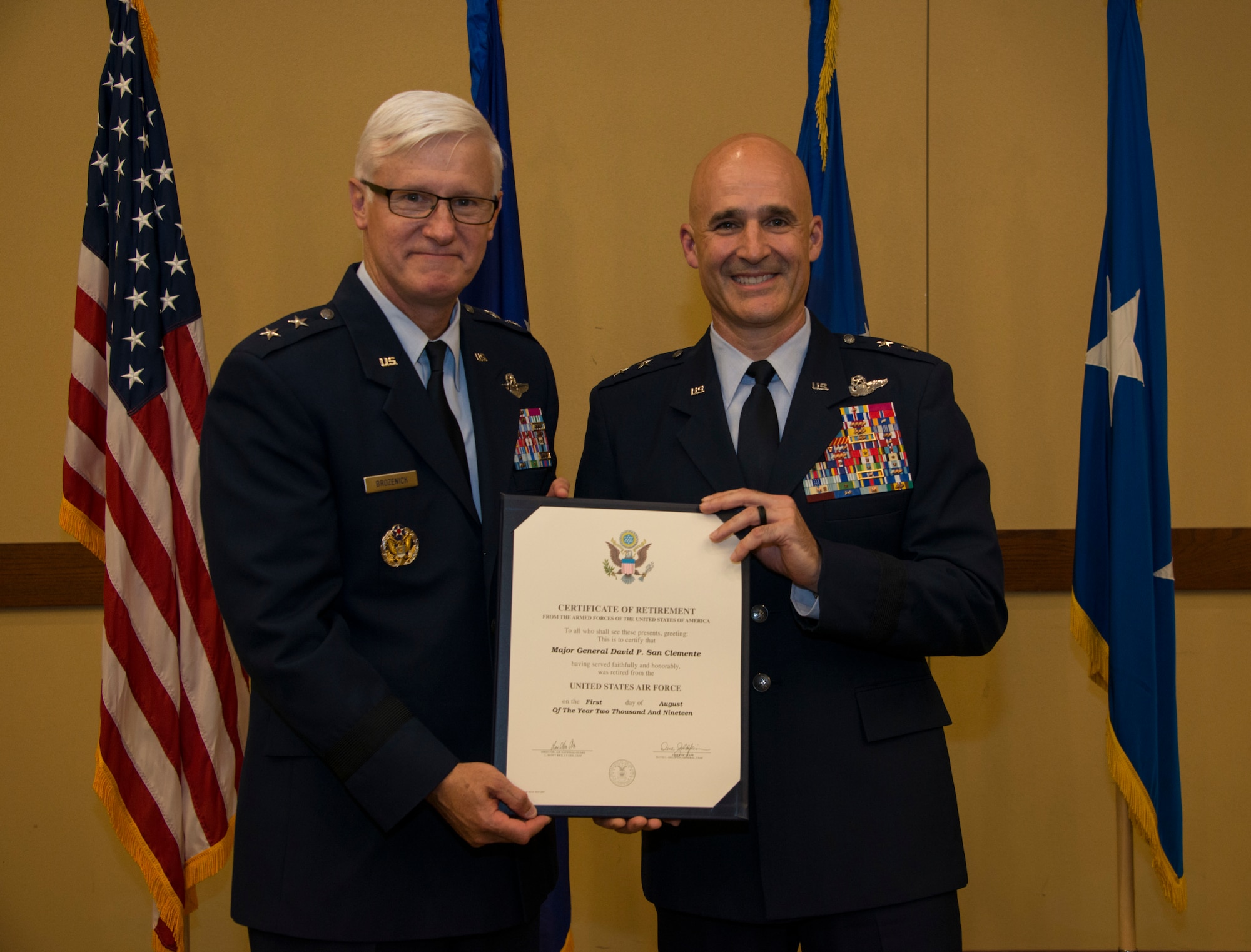 Two people holding a certificate in front of flags.