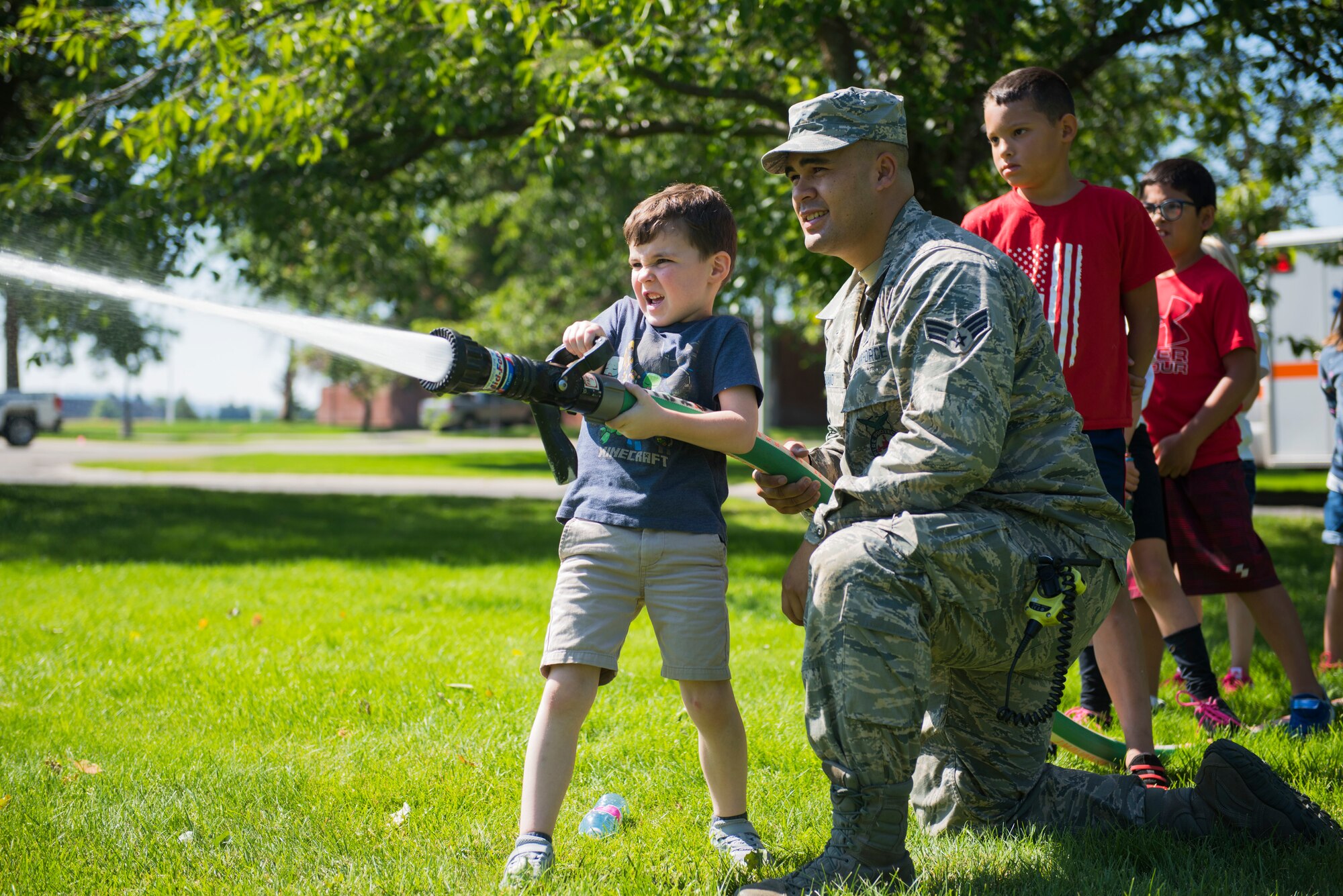 U.S. Air Force Senior Airman Isaiah Raiano, 92nd Civil Engineer Squadron firefighter, helps a child with Fairchild’s Youth Center operate a firehose during the Summer Youth Fair at Fairchild Air Force Base, Washington, July 25, 2019. Approximately 100 children from across Fairchild participated in the fair. (U.S. Air Force photo by Airman 1st Class Lawrence Sena)