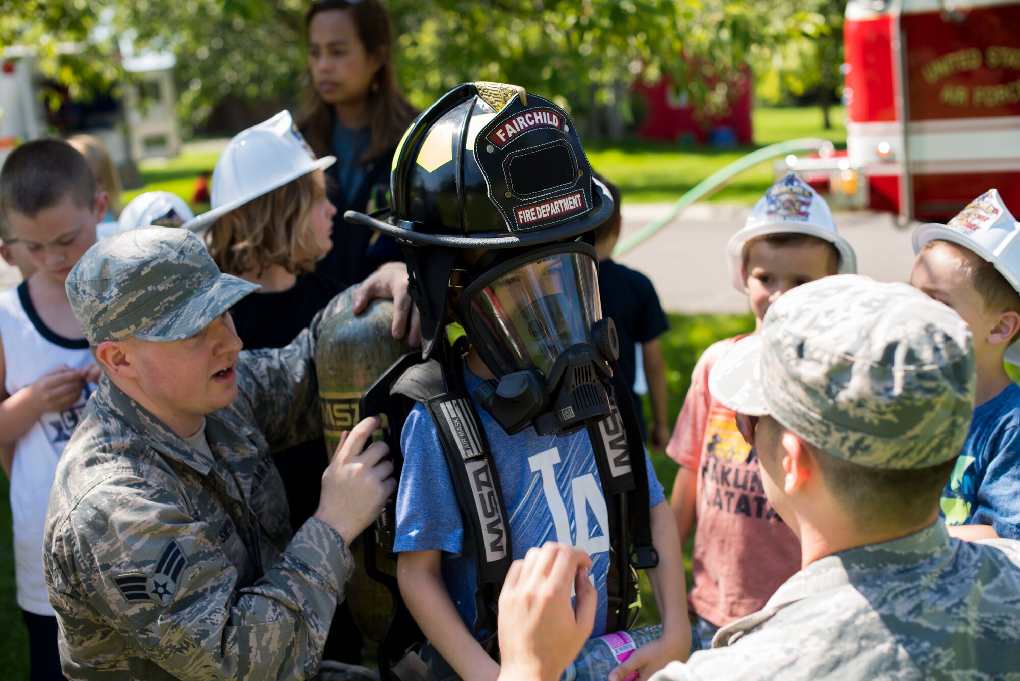 U.S. Air Force Senior Airman Brandon Smith (left) and Senior Airman Andrew Tanner (right), 92nd Civil Engineer Squadron firefighters, assist youth from Fairchild’s Youth Center in trying on equipment during the Summer Youth Fair at Fairchild Air Force Base, Washington, July 25, 2019. Members from Fairchild’s 92nd Civil Engineer Squadron Fire Department, Explosive Ordnance Disposal team, 92nd Security Forces Squadron and 92nd Medical Group provided activities and educational exhibits. (U.S. Air Force photo by Airman 1st Class Lawrence Sena)