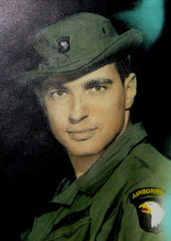 A man wearing a green military uniform with a 101st Airborne Division patch and matching bucket hat looks into the camera.