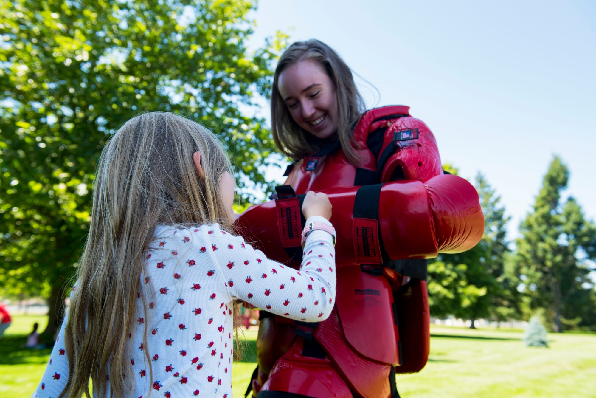 U.S. Air Force Senior Airman Samantha Rucker, 92nd Security Forces Squadron administrator, demonstrates the effectiveness of a “Redman Suit”, a physical combat training aid, to a kid from Fairchild’s Youth Center during the Summer Youth Fair at Fairchild Air Force Base, Washington, July 25, 2019. Approximately 100 children from across Fairchild participated in the fair. (U.S. Air Force photo by Airman 1st Class Lawrence Sena)