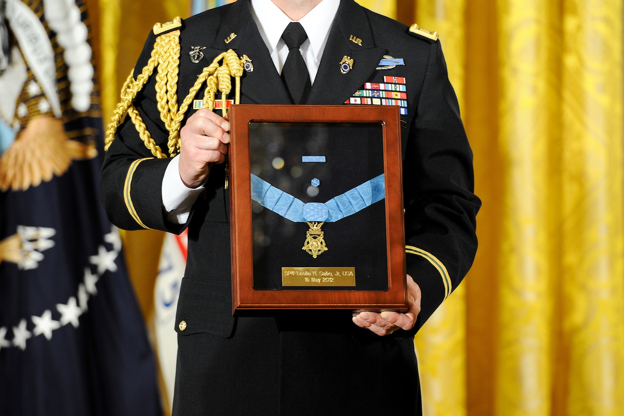 A soldier in dress uniform holds a case enshrining a Medal of Honor.
