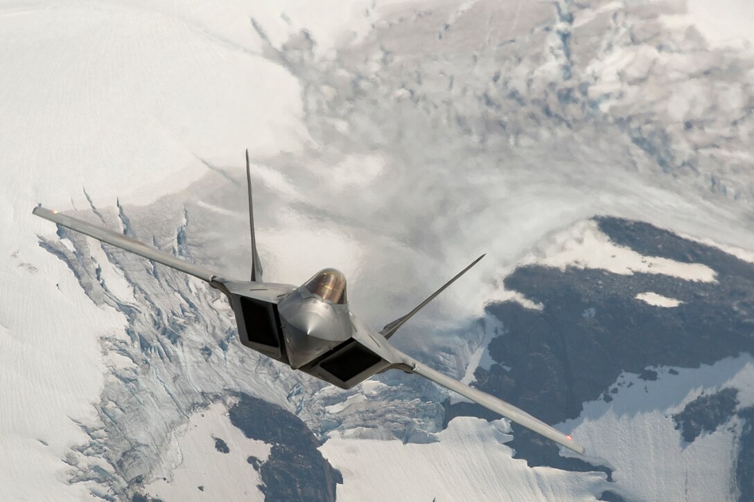 An F-22 Raptor flies over snowy terrain.