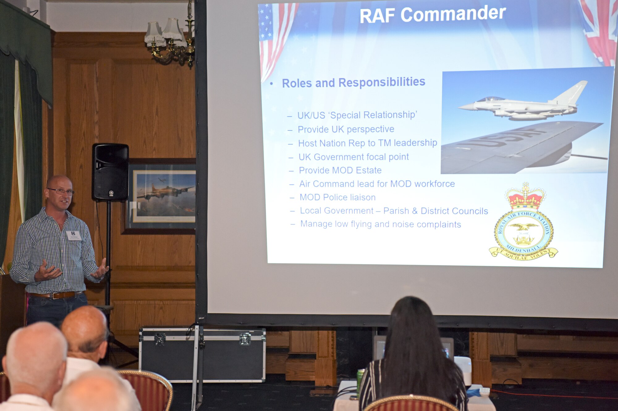 Squadron Leader Paul Graham, RAF Mildenhall station commander, delivers a briefing to local community leaders during the New Mayors’ Barbecue at RAF Mildenhall, England, July 27, 2019. The annual event hosted by the U.S. Air Force Col. Troy Pananon, 100th Air Refueling Wing commander, consisted of wing mission and economic impact briefs, a KC-135 Stratotanker nose art-themed lunch and friendly games of cornhole. (U.S. Air Force photo by Airman 1st Class Brandon Esau)