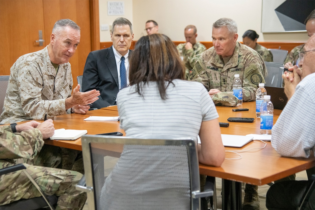 Military leaders and media members talk around a table.