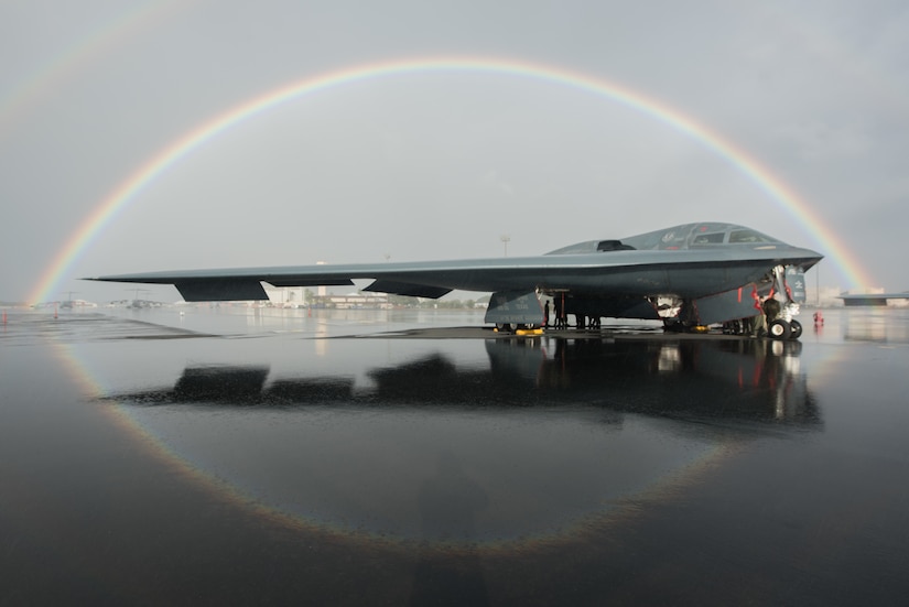 A B-2 Spirit bomber sits on the flight line in Hawaii. A rainbow encircles it.