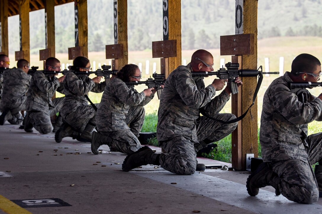 A group of airmen kneeling in a line pointing their weapons toward a target.