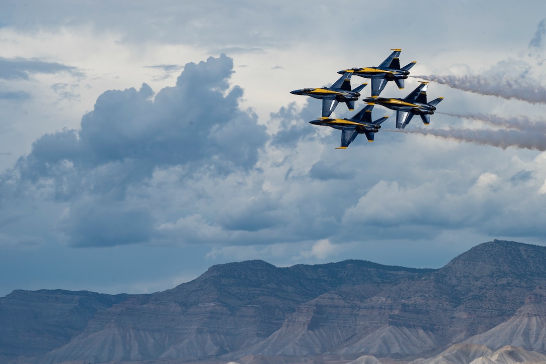 The Blue Angels perform at an airshow with mountains in the background.