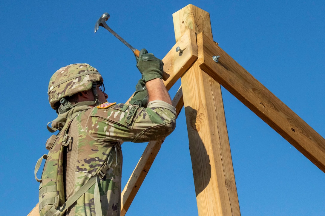 A soldier hammers a nail into a wooden beam.