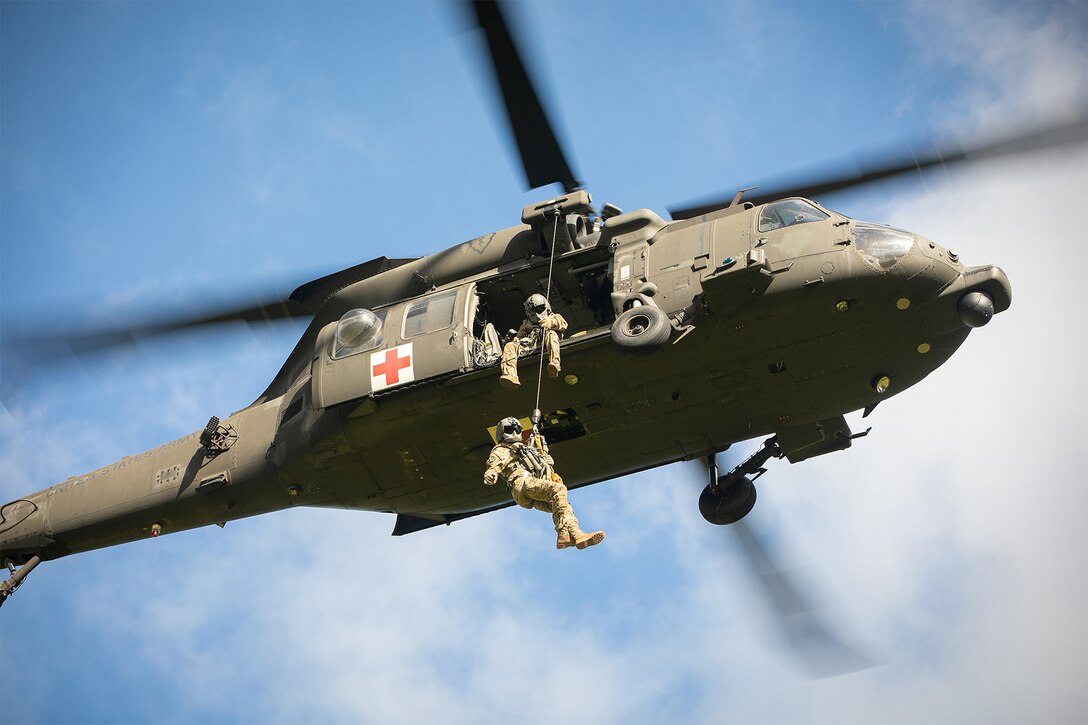 Soldiers hold on to a rope as they come out of a helicopter.