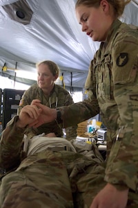 Maj. Andrea Hickman, of Des Moines, Iowa, a family medicine physician, and Pfc. Madison Huggins, of Sioux City, Iowa, a combat medic specialist with Headquarters and Headquarters Troop, 1st Battalion, 113th Cavalry Regiment, 2nd Infantry Brigade Combat Team, 34th Infantry Division, Iowa Army National Guard (IANG), check a simulated casualty for hemorrhaging in their initial trauma treatment during a 21-day eXportable Combat Training Capability (XCTC) rotation at Camp Ripley, Minn., on July 23, 2019.