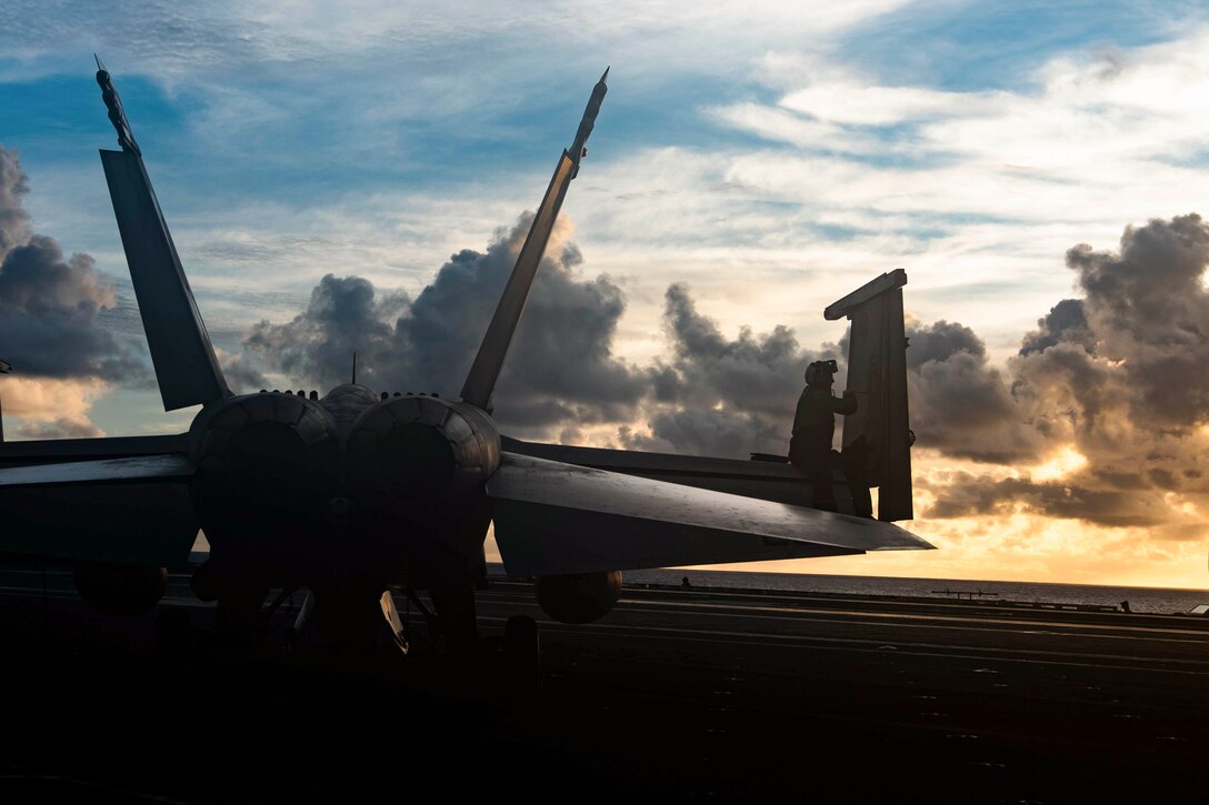 A sailor works on an aircraft while sitting on the wing.