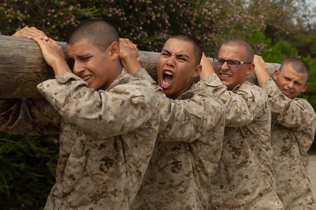 Four service members carry a large log.