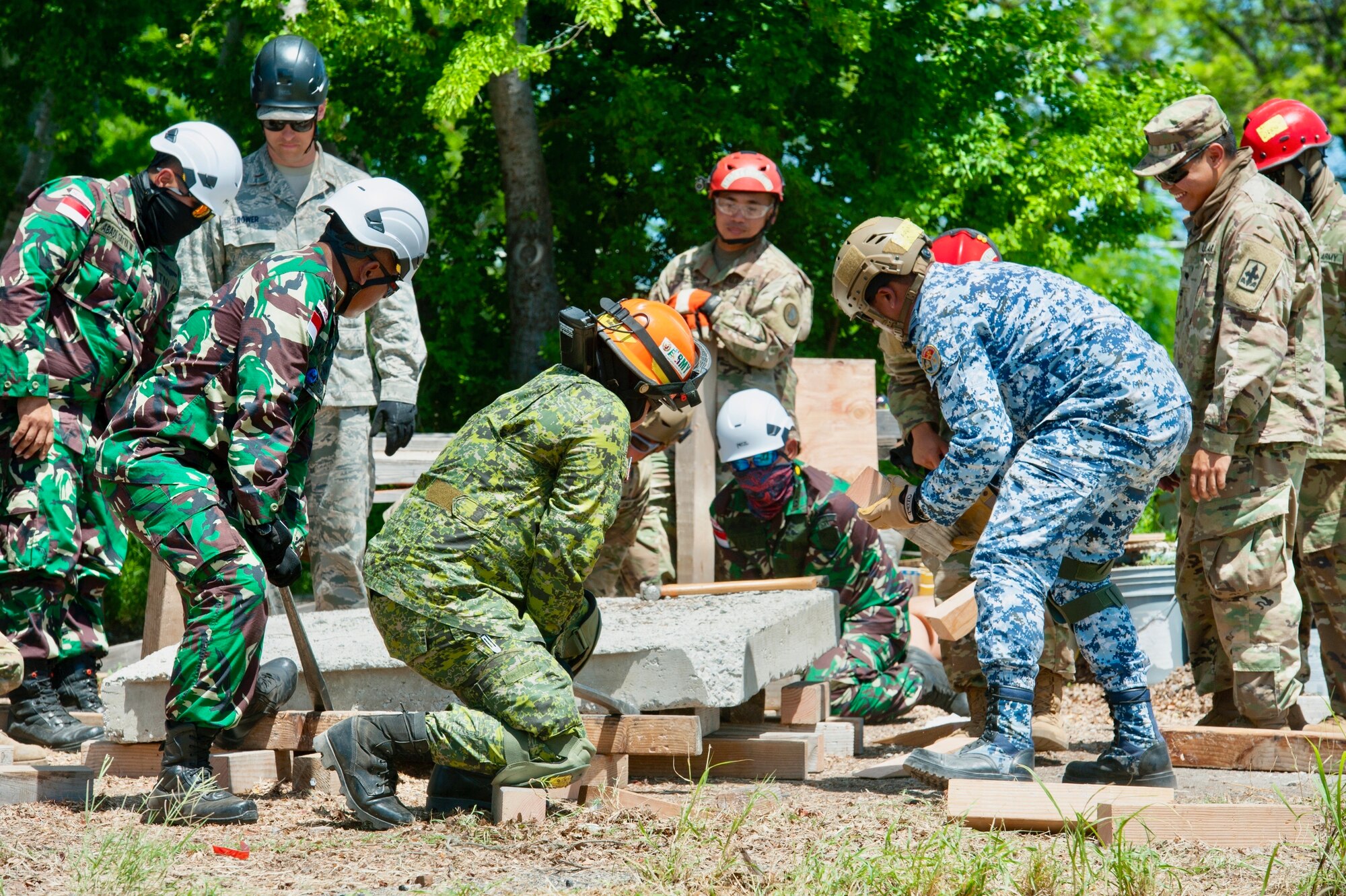 Service members from multiple nations lift up a large cement block during breaching and shoring training as part of the combined - Multinational Task Force [CTF 501] search and extraction training exercise on July 18, 2019 at Kalaeloa Urban Search and Rescue Training area, Hawaii.