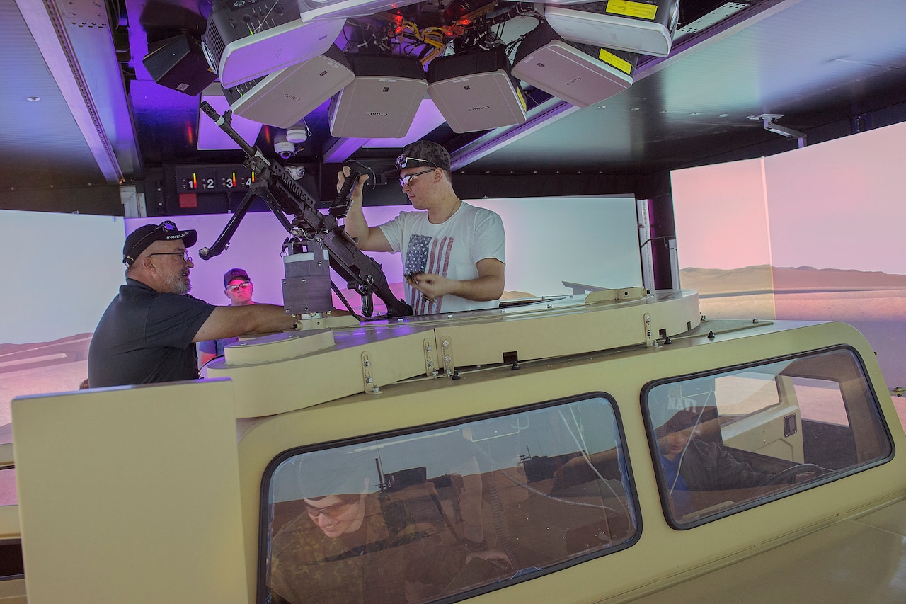 Two men emerge from the top of a military combat vehicle simulator.
