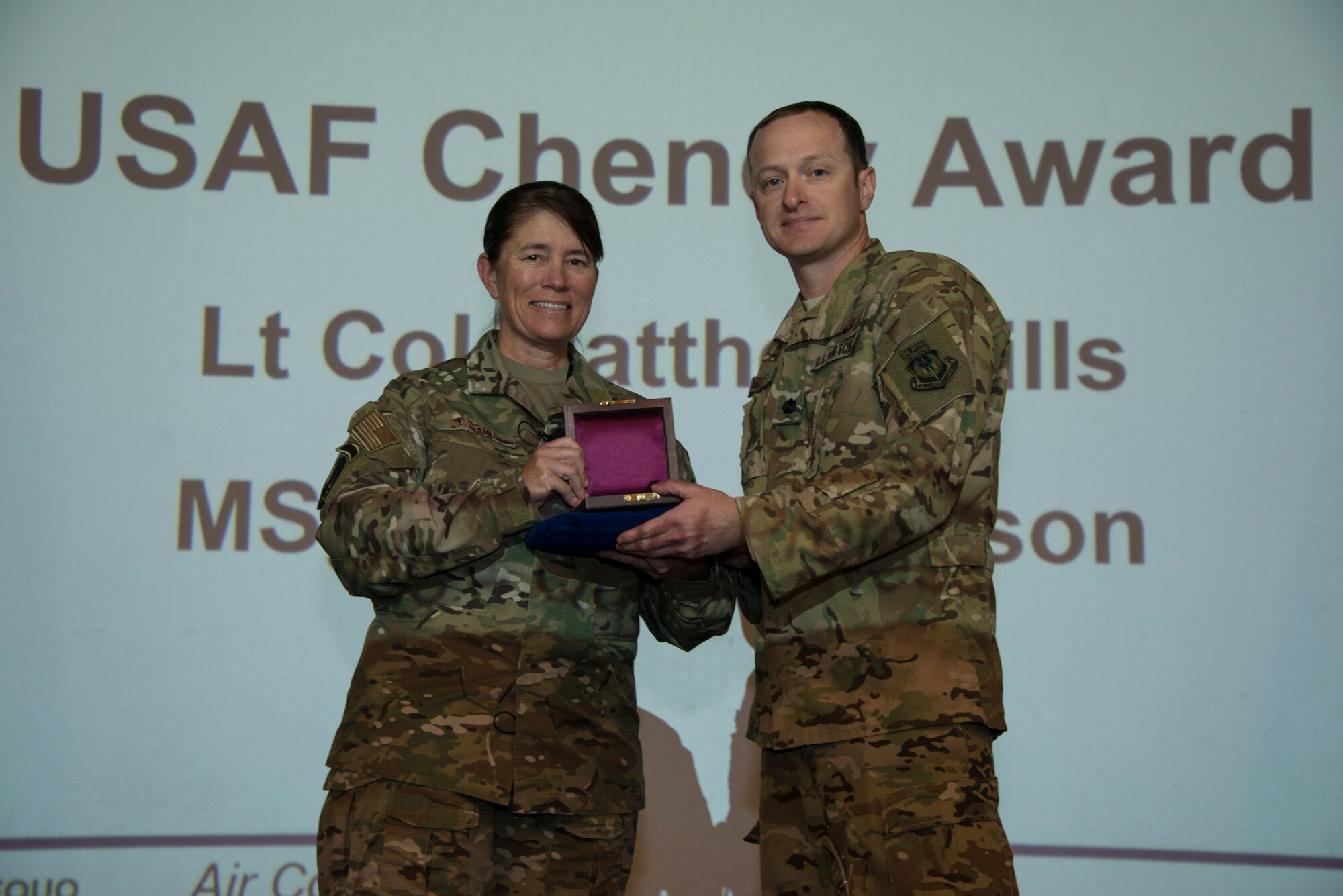 Two people holding an award in front of a screen.