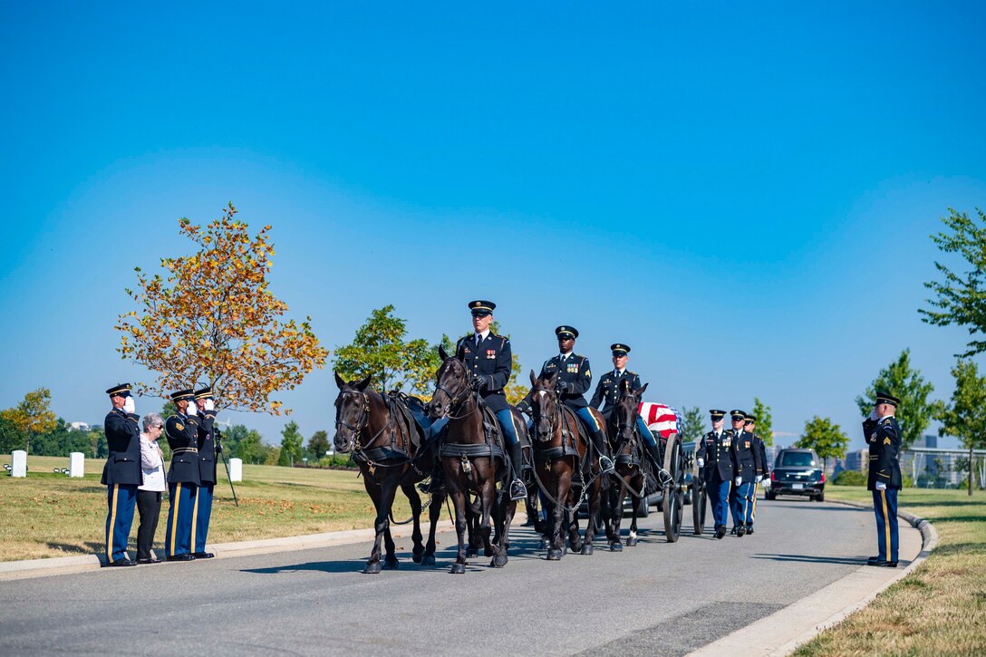 Soldiers on horses lead a funeral procession at a cemetery.