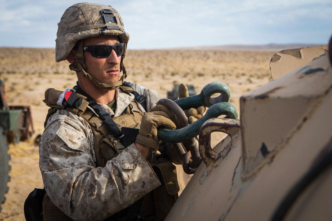 A Marine attaches a shackle to a vehicle.